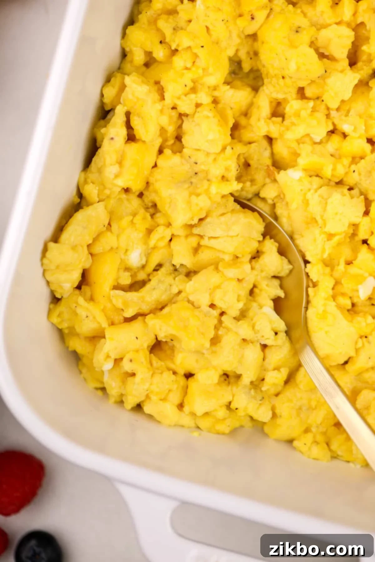 Scooping scrambled eggs from a baking dish.