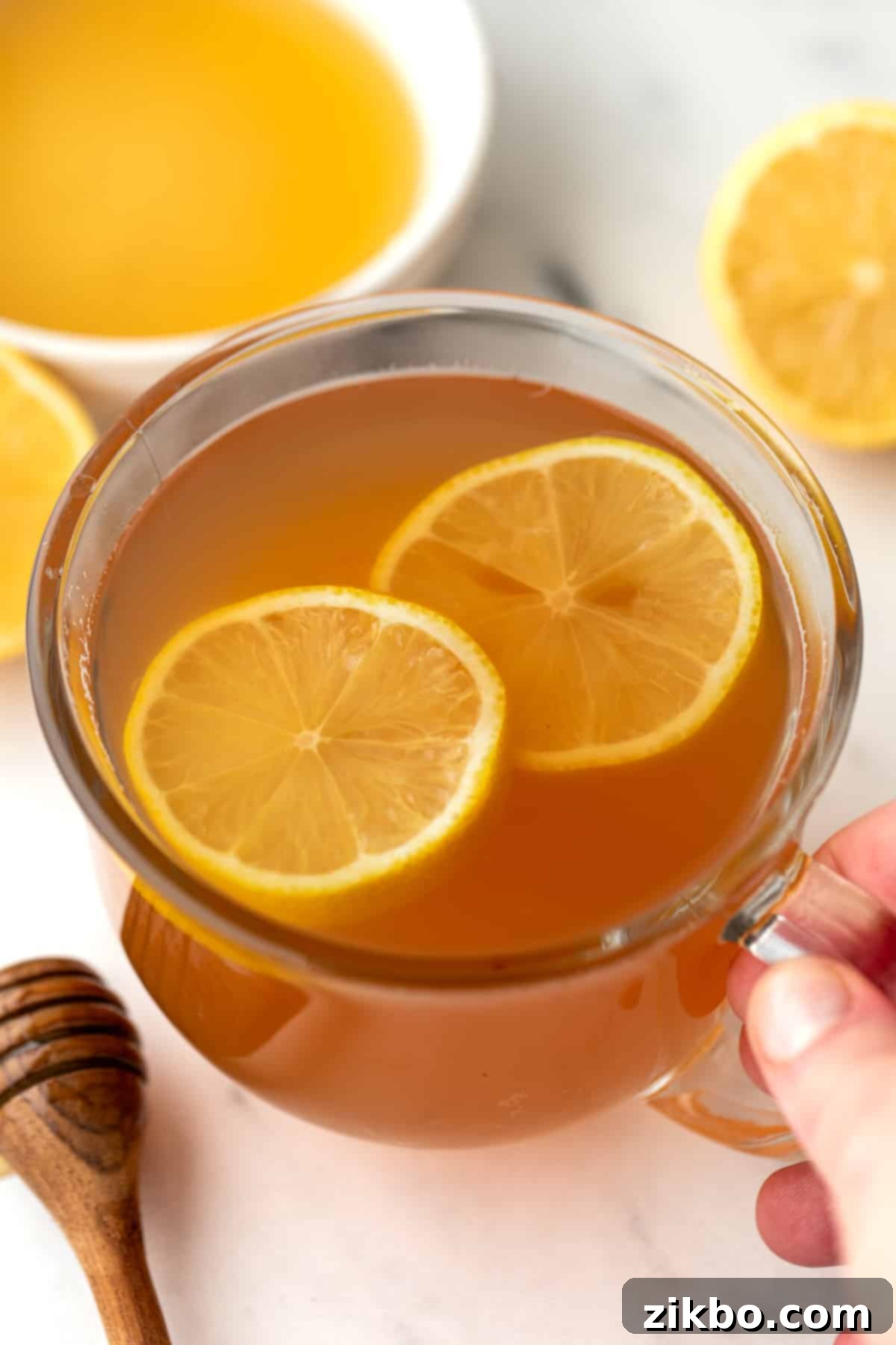 A glass mug filled with golden-hued tea and garnished with fresh lemon slices, ready to provide comfort.