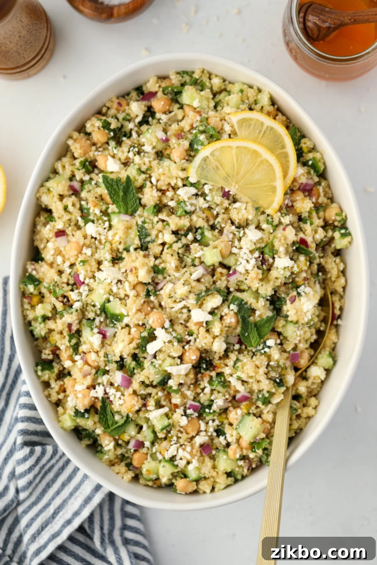 A large salad bowl filled with a bright quinoa salad garnished with lemon slices and fresh mint.