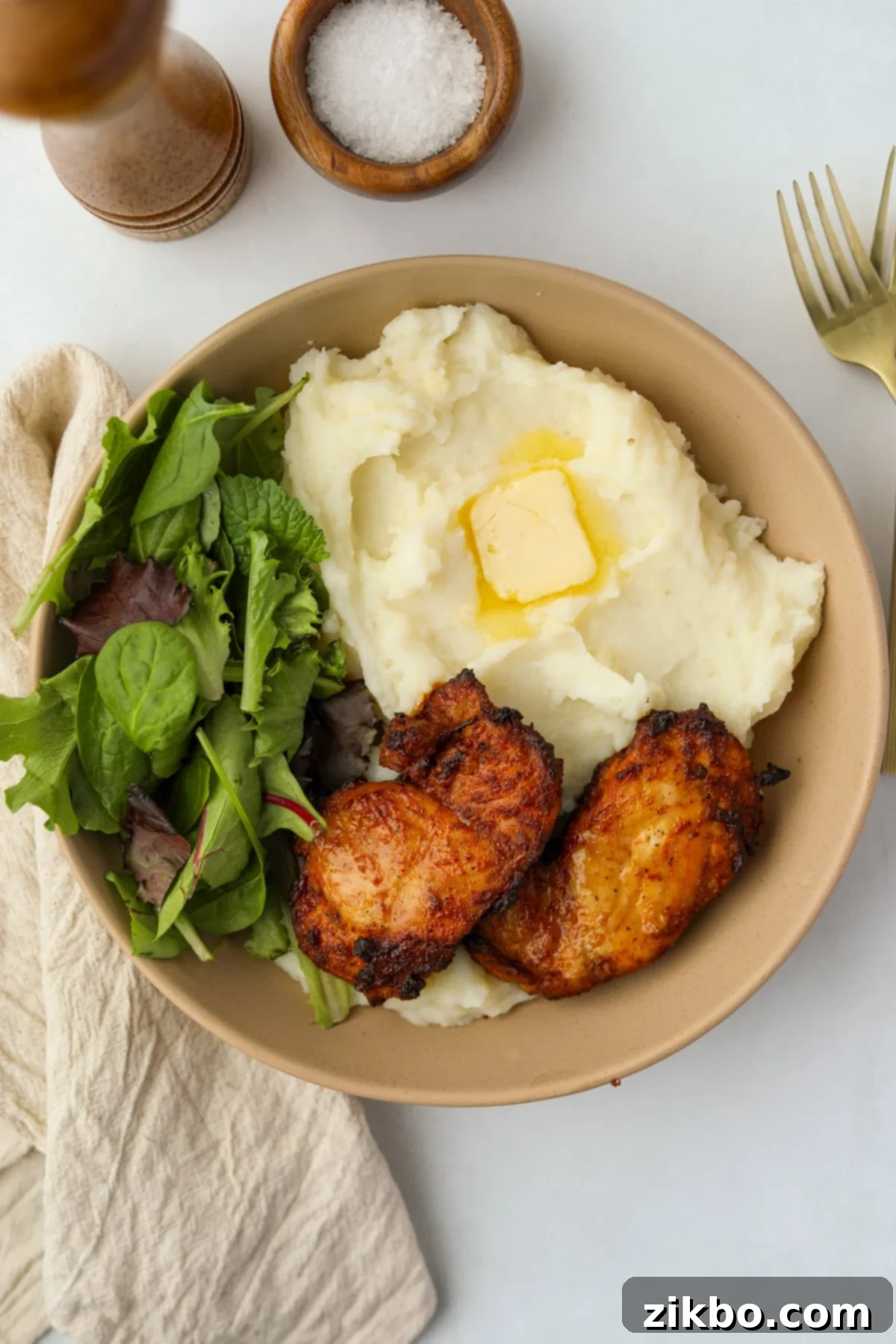 Crispy and Juicy Air Fryer Chicken Thighs 5 A shallow bowl featuring salad, mashed potatoes, melted butter, and crispy chicken thighs.