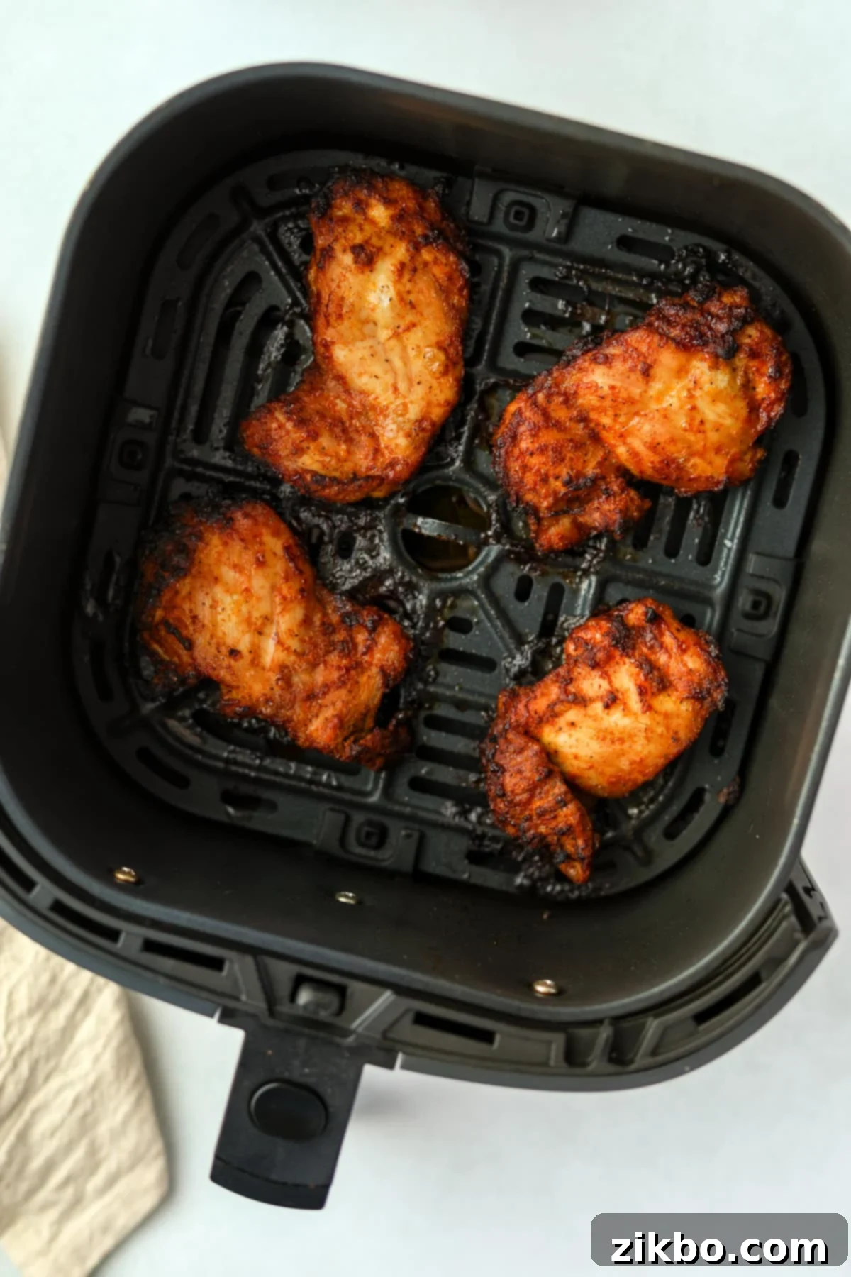 Crispy and Juicy Air Fryer Chicken Thighs 6 An air fryer basket with cooked chicken thigh pieces.