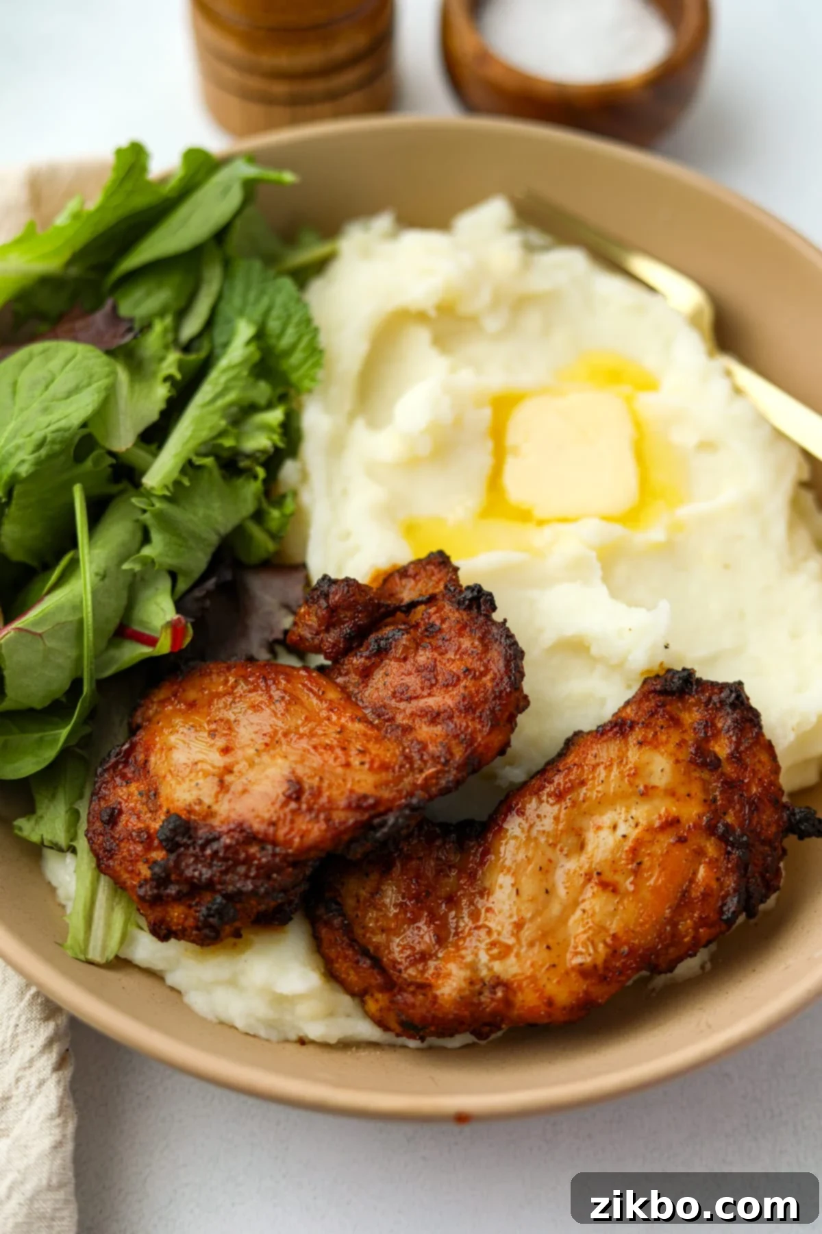 Crispy and Juicy Air Fryer Chicken Thighs 7 A close up of two cooked chicken thighs on a bed of mashed potatoes.
