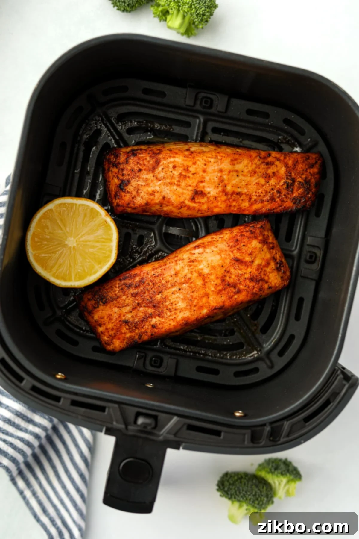 An air fryer basket with two cooked salmon fillets inside, garnished with fresh herbs and lemon wedges.