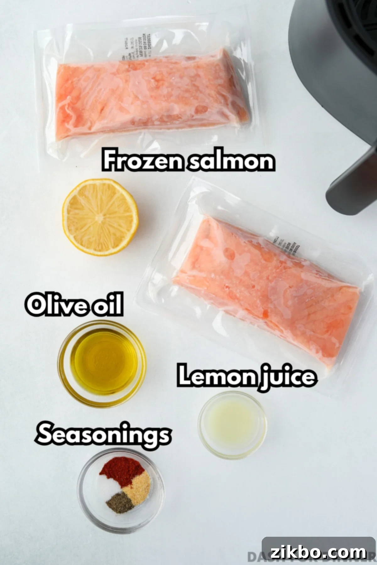 Two fillets of frozen salmon that are vacuum packed, plus olive oil, lemon, and seasonings laid out on a kitchen counter.