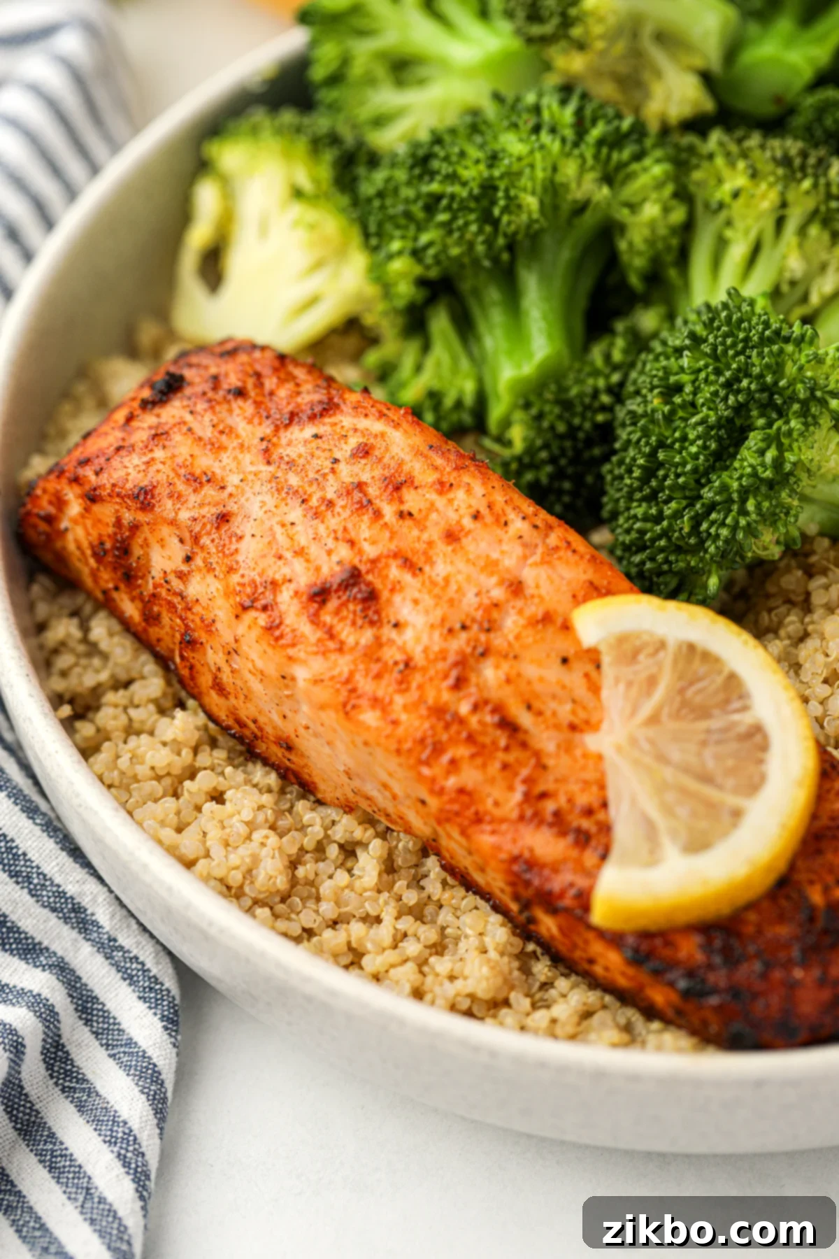 A close-up of a perfectly cooked salmon fillet on a bed of quinoa, surrounded by vibrant steamed broccoli.