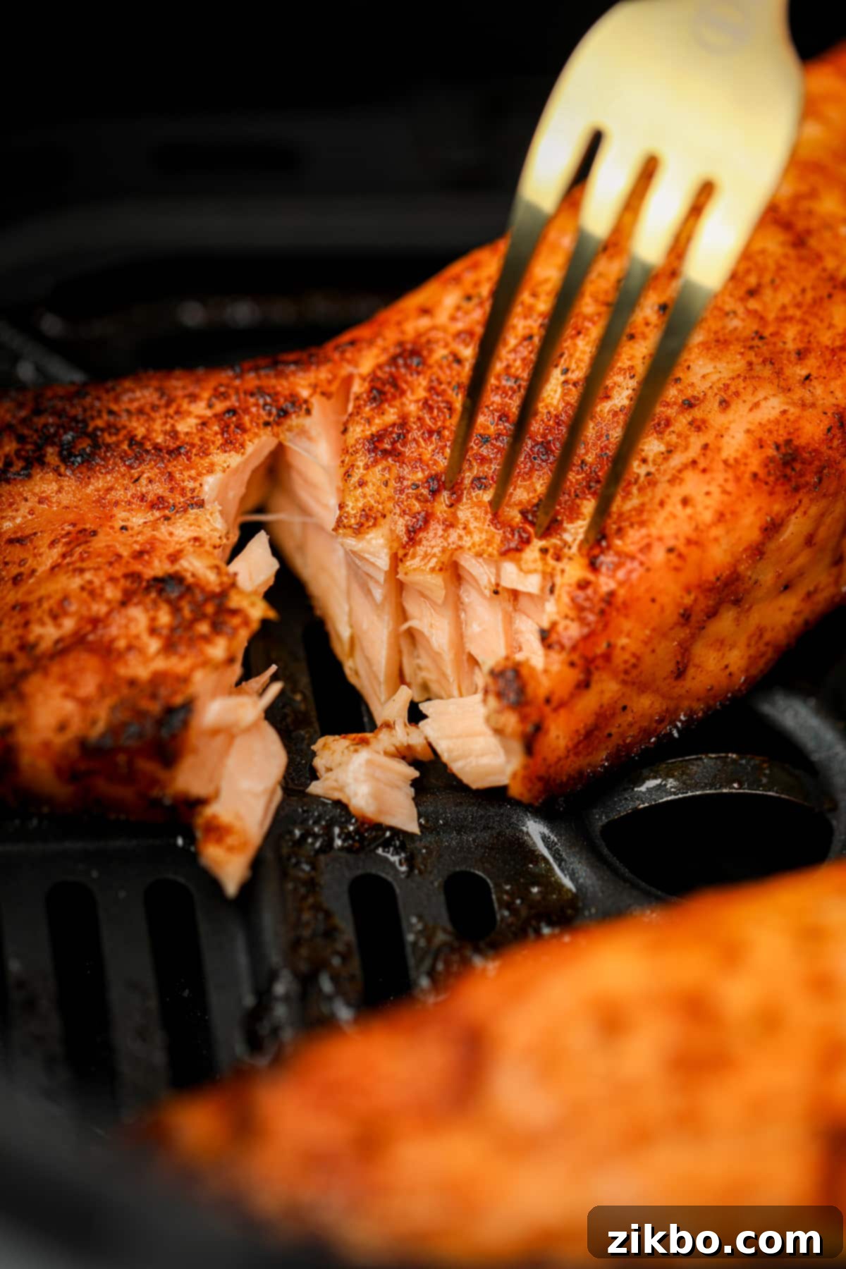 A fork flaking a piece of cooked salmon to expose the juicy, tender insides, showcasing its perfect doneness.