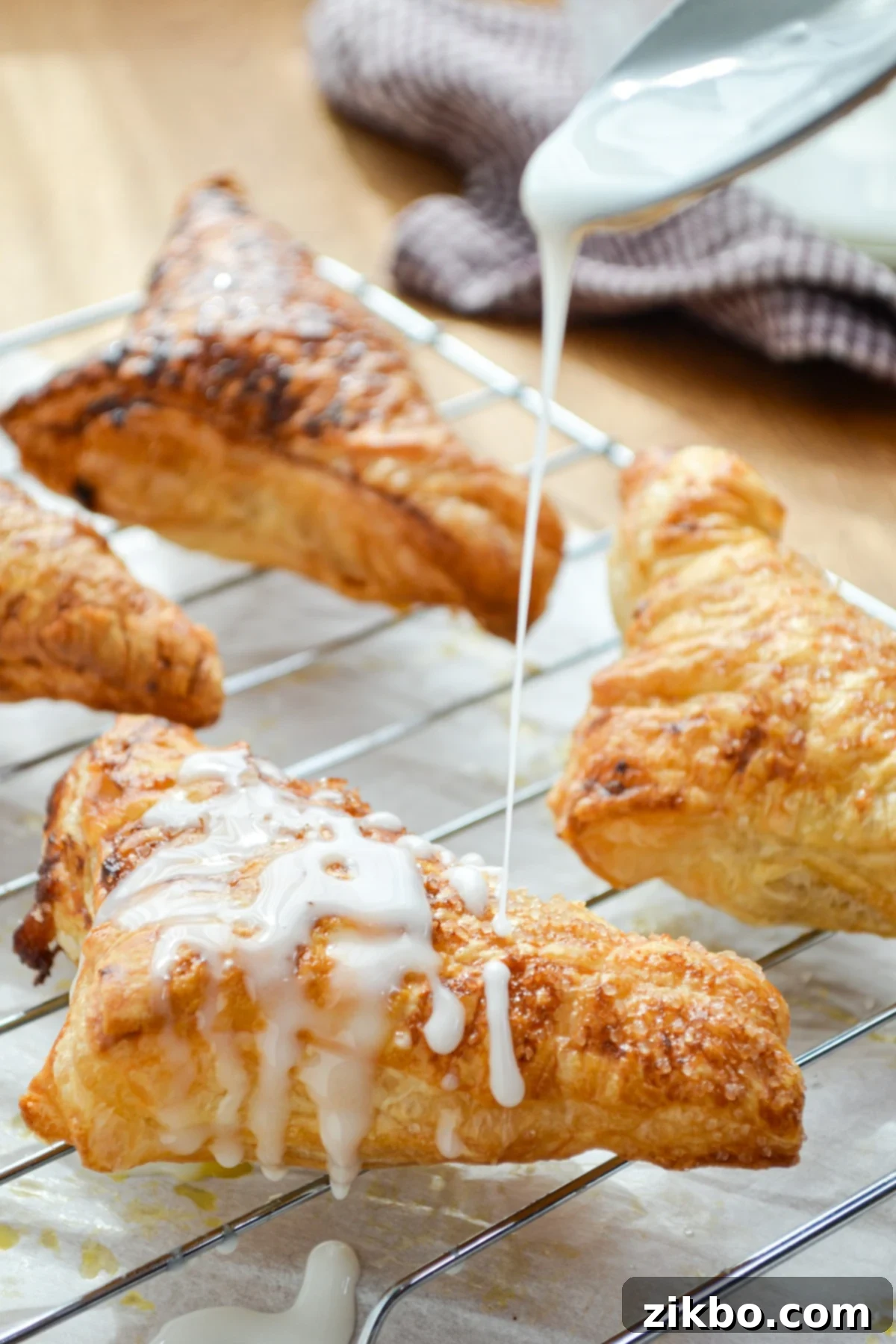 A perfectly baked apple turnover being drizzled with a simple, sweet glaze.
