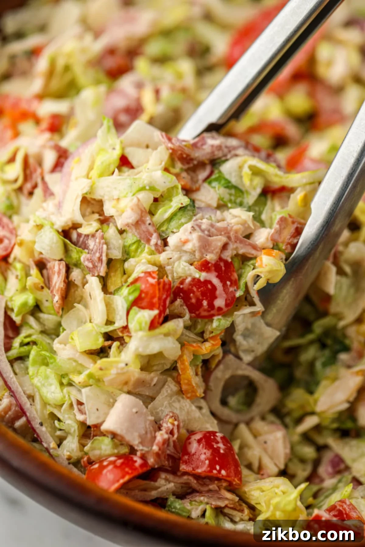 Tongs taking a portion of chopped salad from a large wooden bowl.