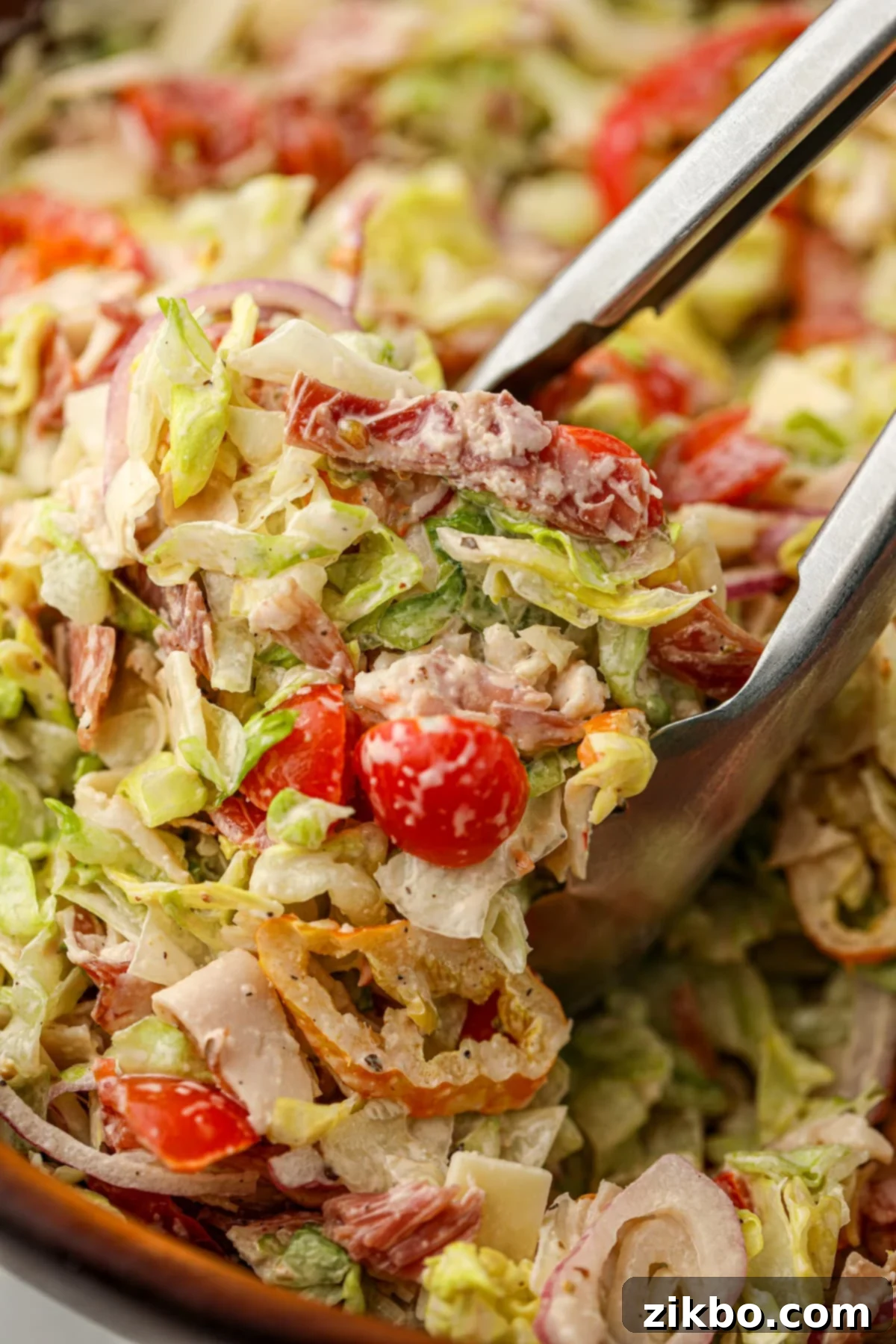 Scooping a portion of chopped salad with a large pair of tongs.