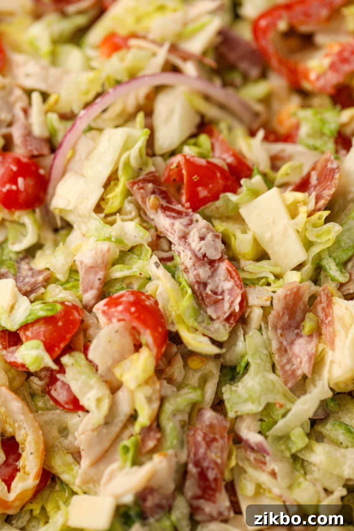 A close up on grinder salad, showing pieces of deli meat, cherry tomatoes, red onion, and banana pepper.