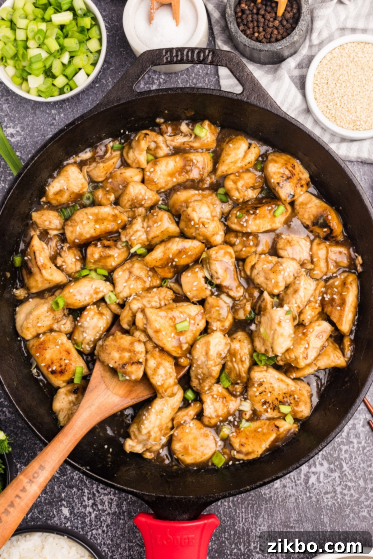 A cast iron skillet filled with chicken stir fry, being scooped with a wooden spoon.