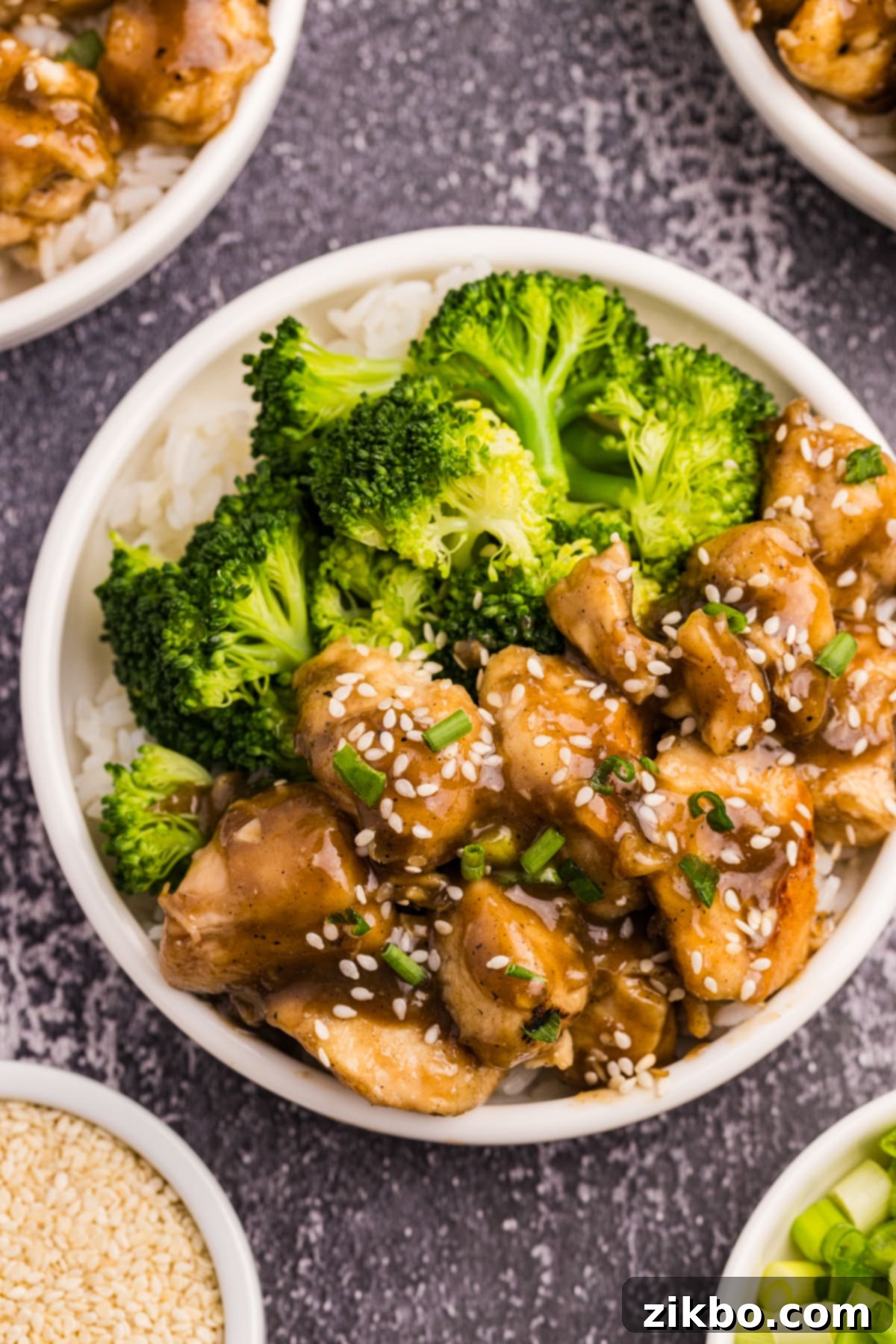 A bowl of rice topped with cooked chicken in sauce and steamed broccoli.