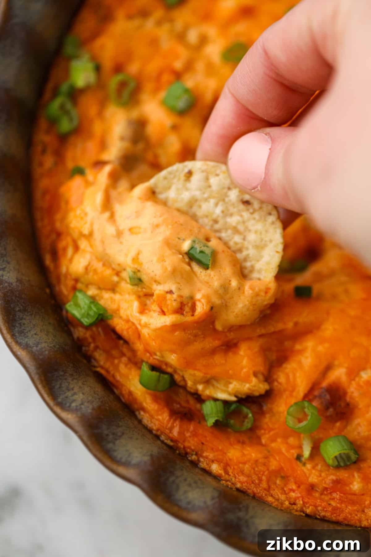 Dipping a tortilla chip into a cheesy buffalo dip.
