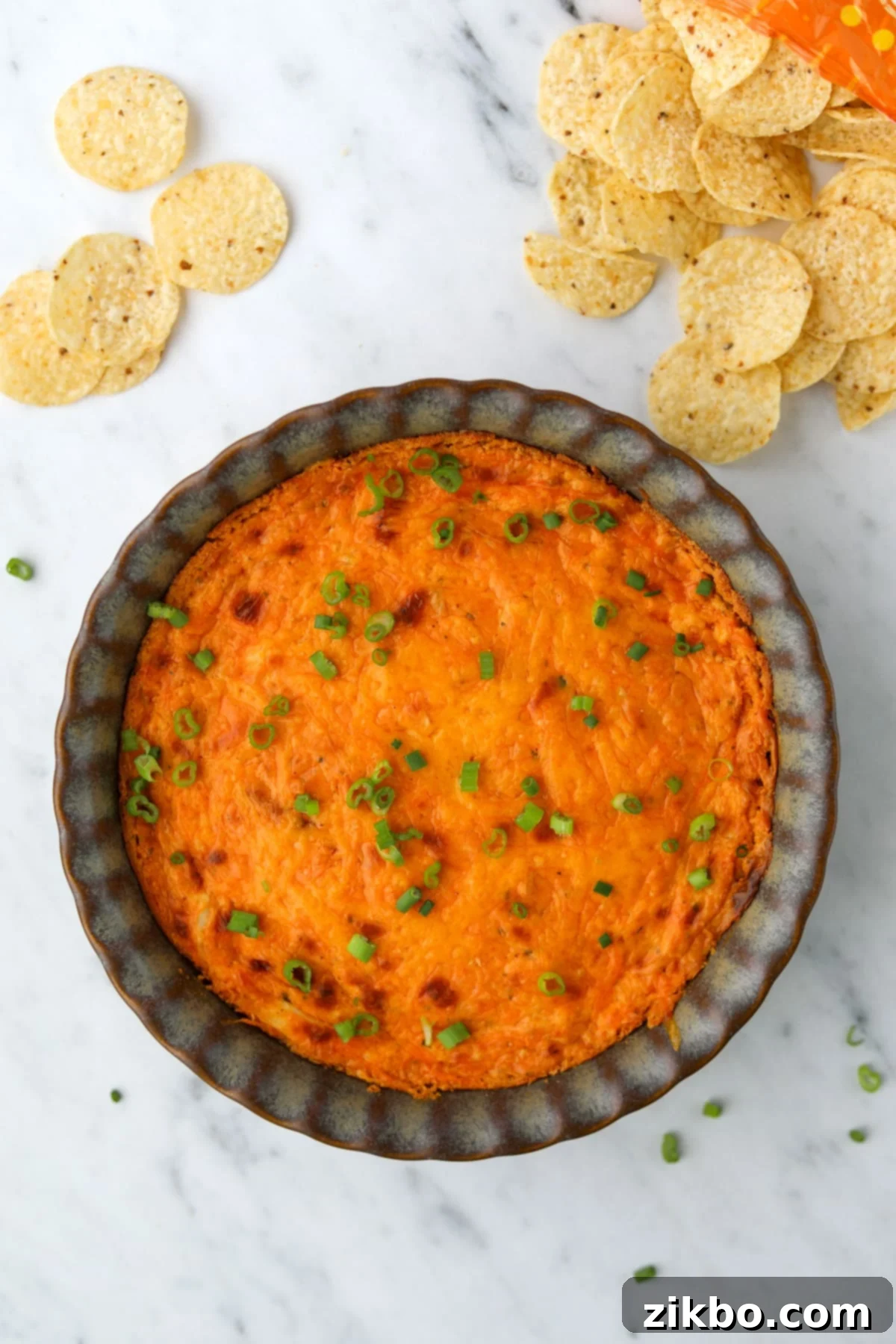 A brightly colored buffalo chicken dip in a pie plate, surrounded by tortilla chips.