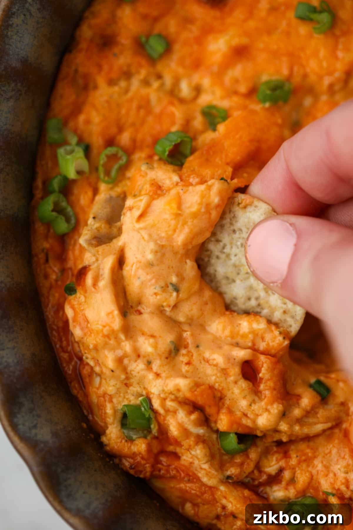 Dipping a tortilla chip into a brightly colored buffalo chicken dip.