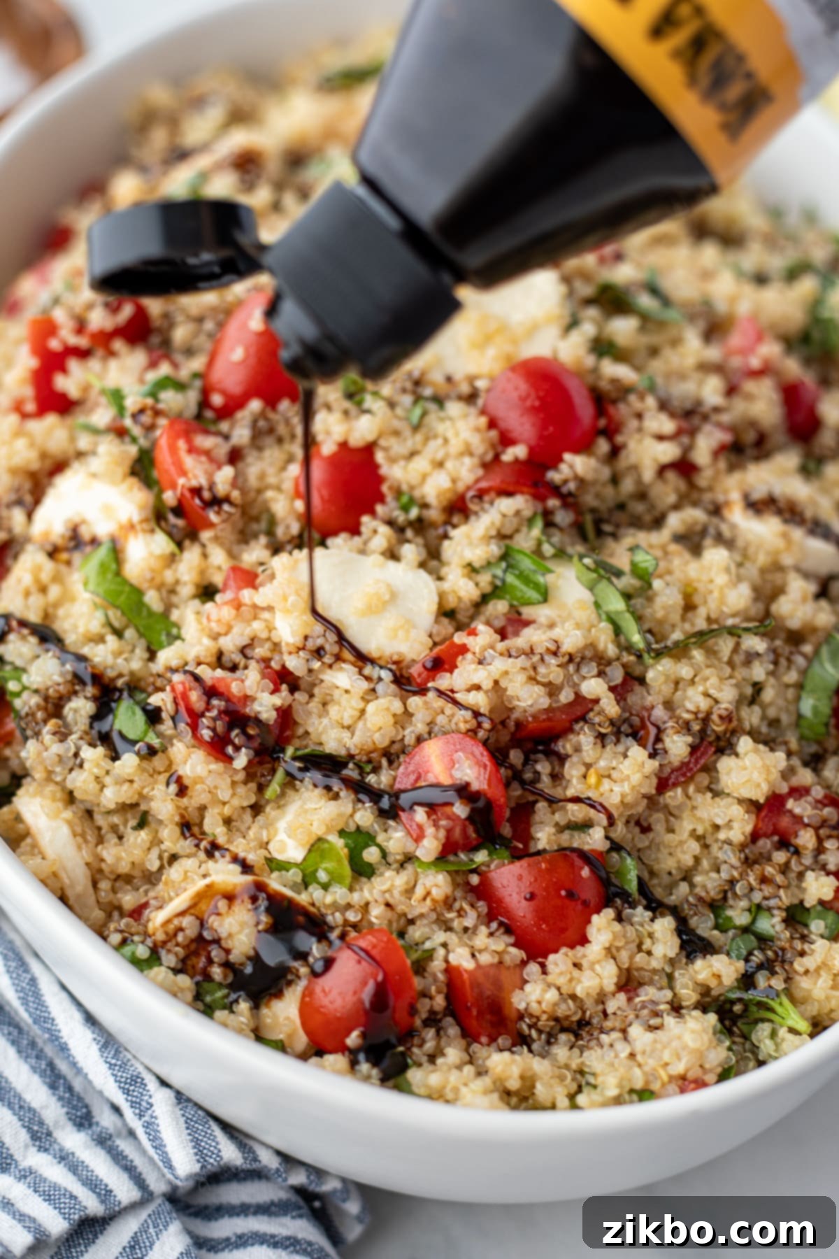 Fresh Caprese Quinoa 5 Balsamic glaze being drizzled on top of a quinoa salad in a large serving bowl.