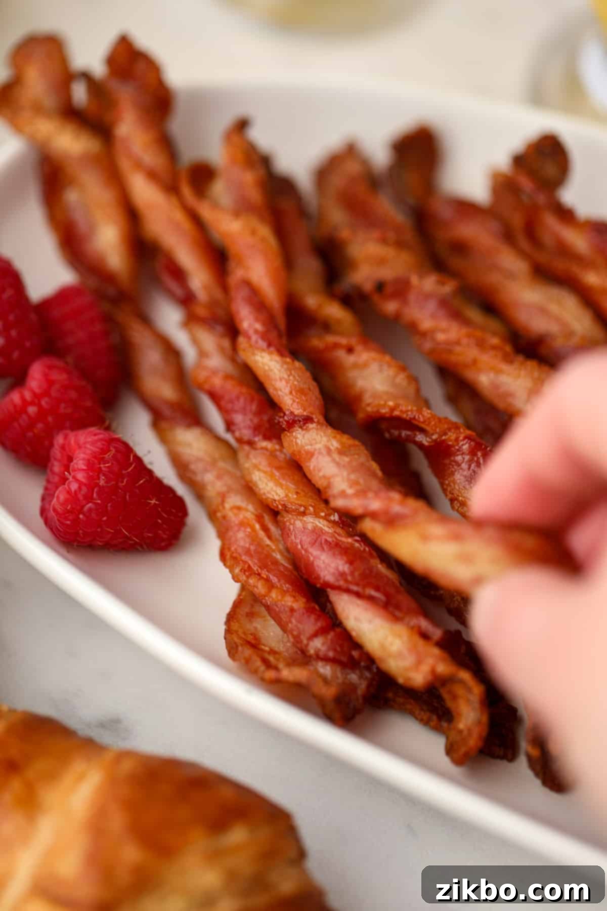 A hand taking a single bacon twist from a large platter full.