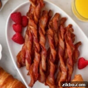 A platter full of twisted bacon/bacon twists, garnished with fresh raspberries.
