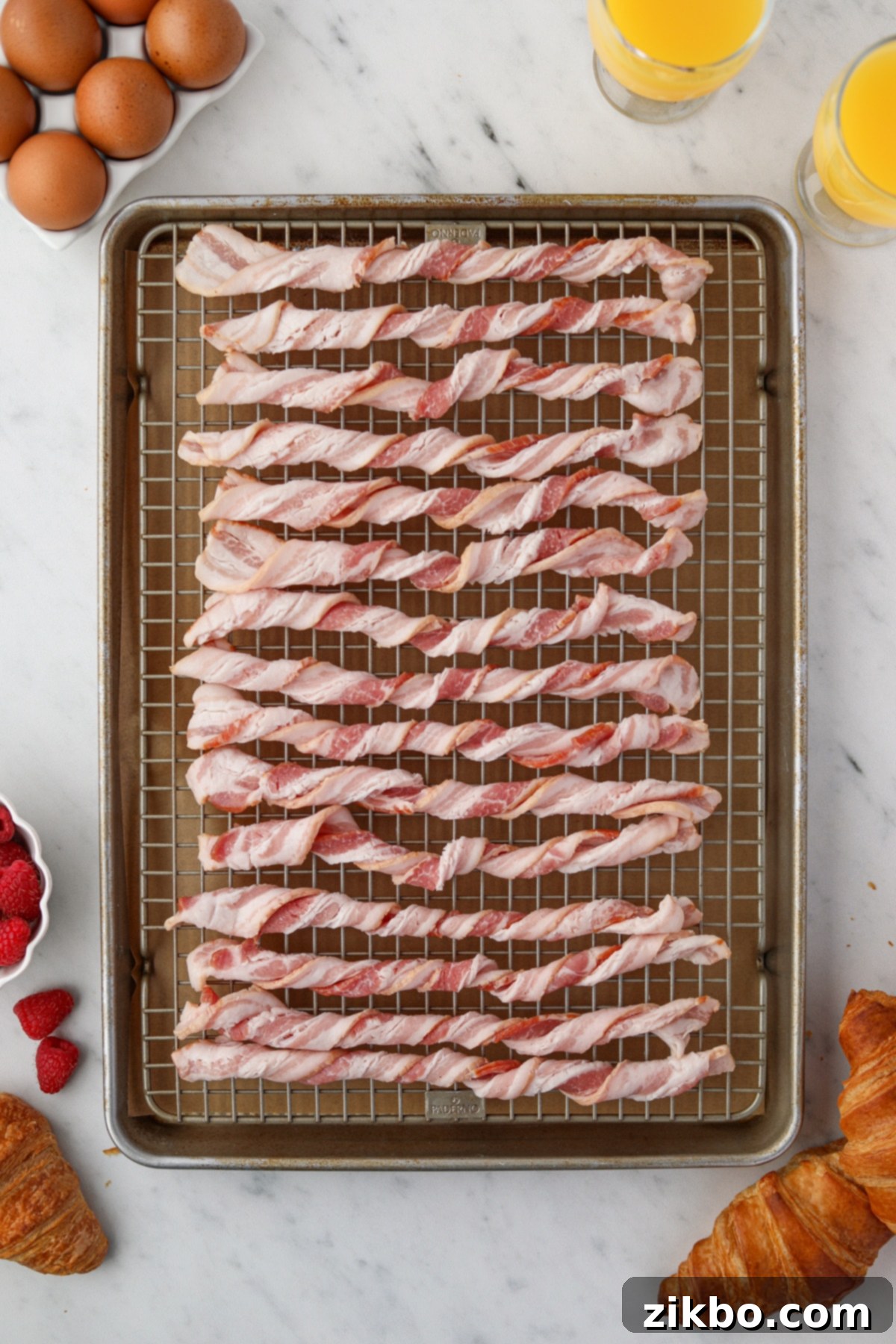 A baking sheet with a wire baking rack filled with twisted raw bacon slices.