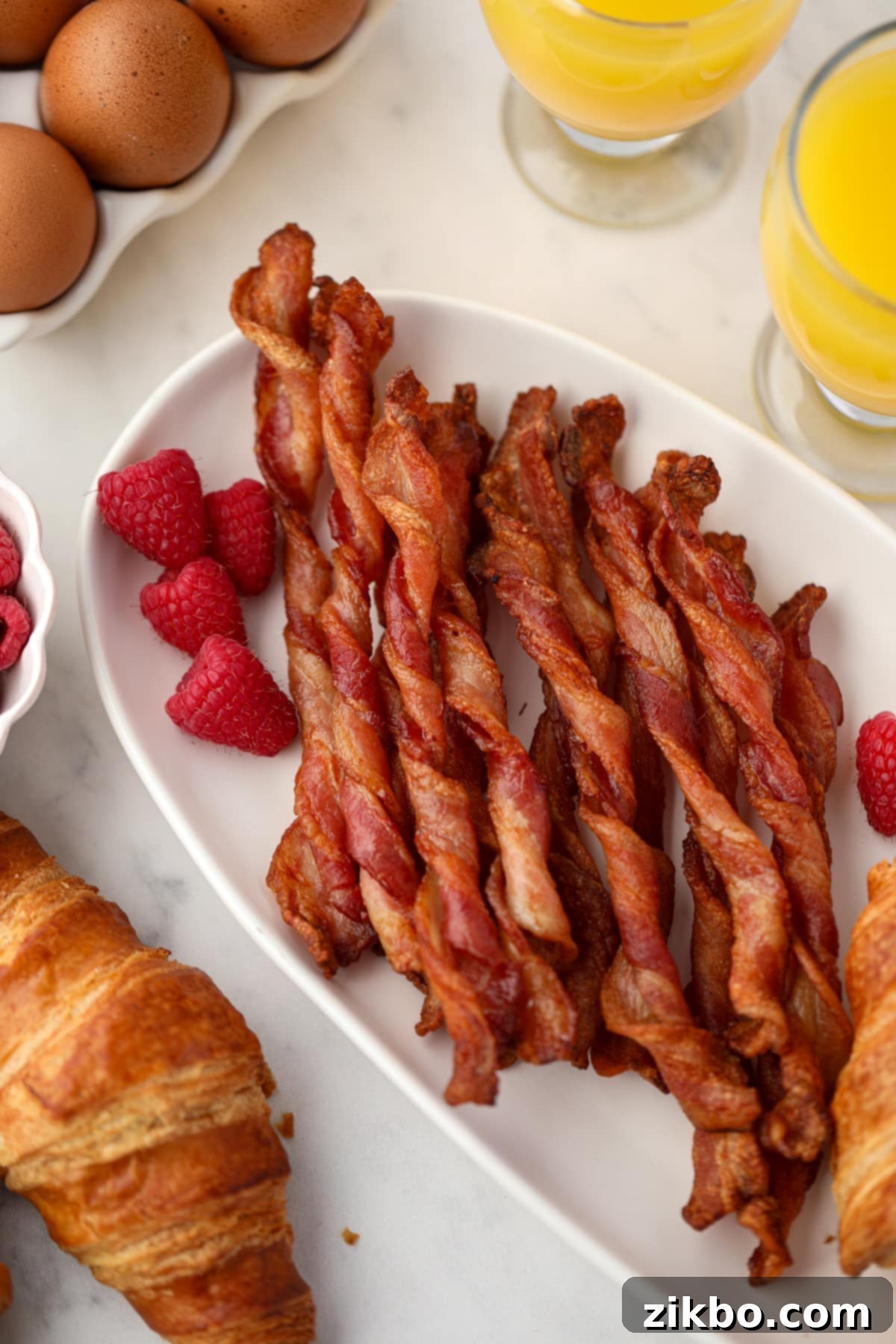 A platter of twisted bacon pieces, garnished with fresh raspberries.