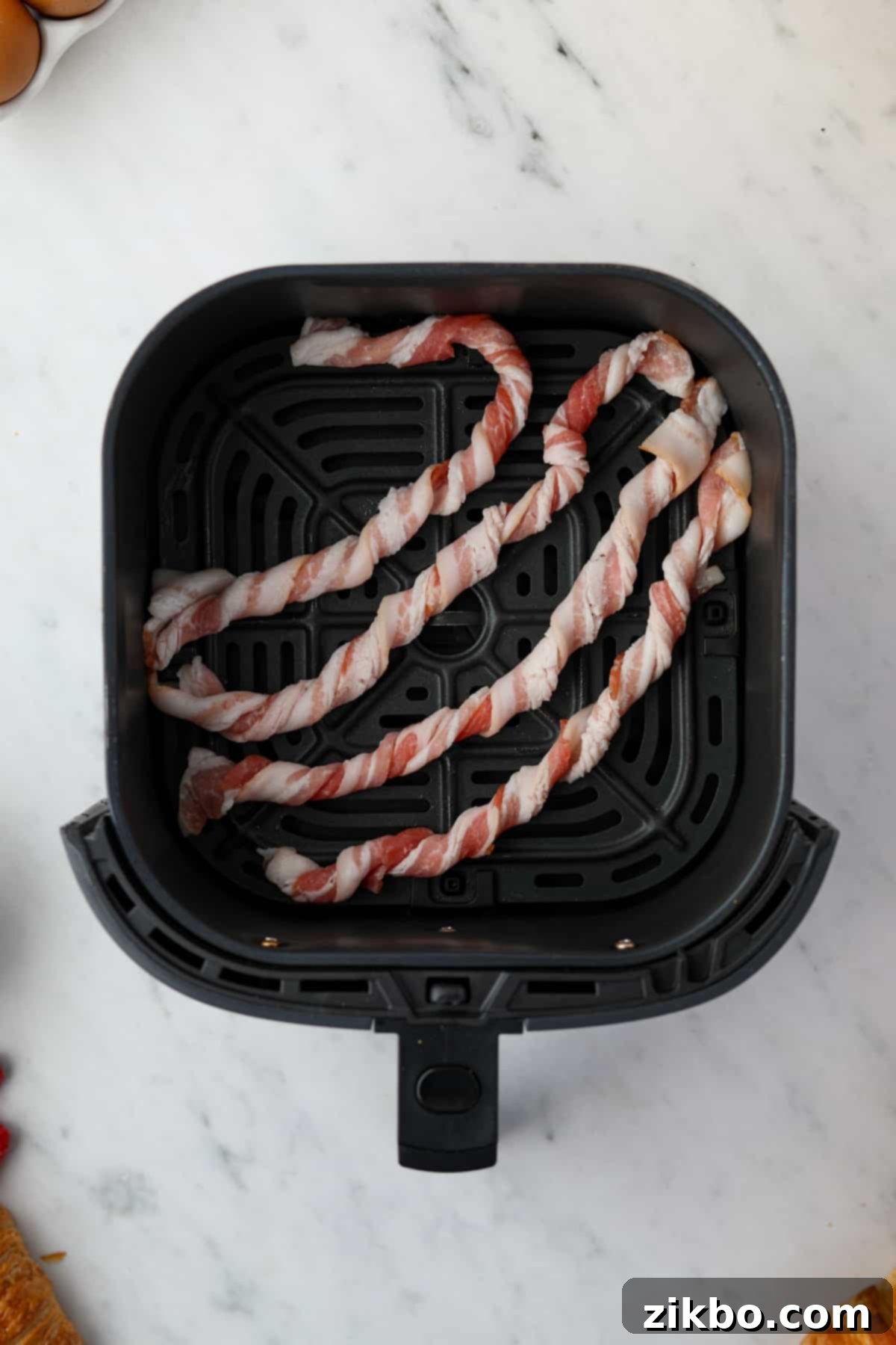 An air fryer with 4 bacon spirals set inside, bent slightly.