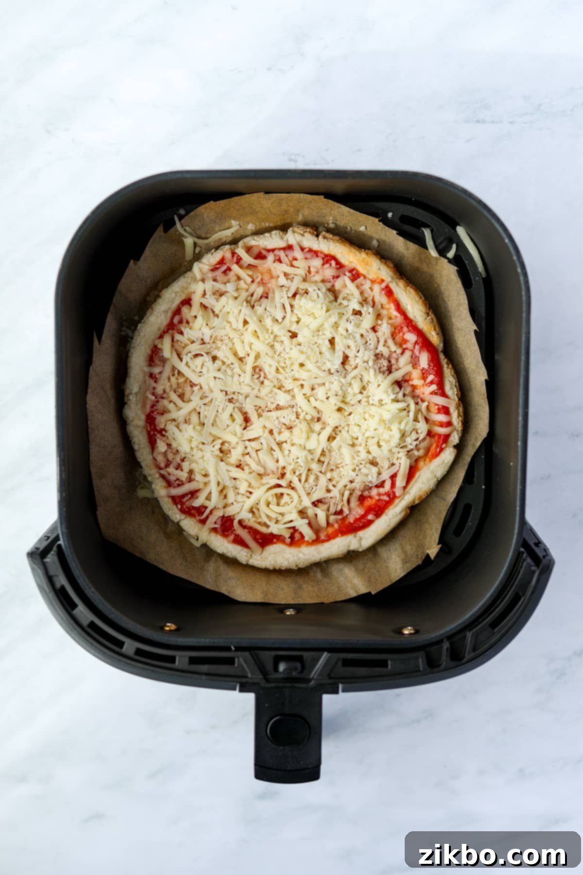 An air fryer with an uncooked mini pizza inside.
