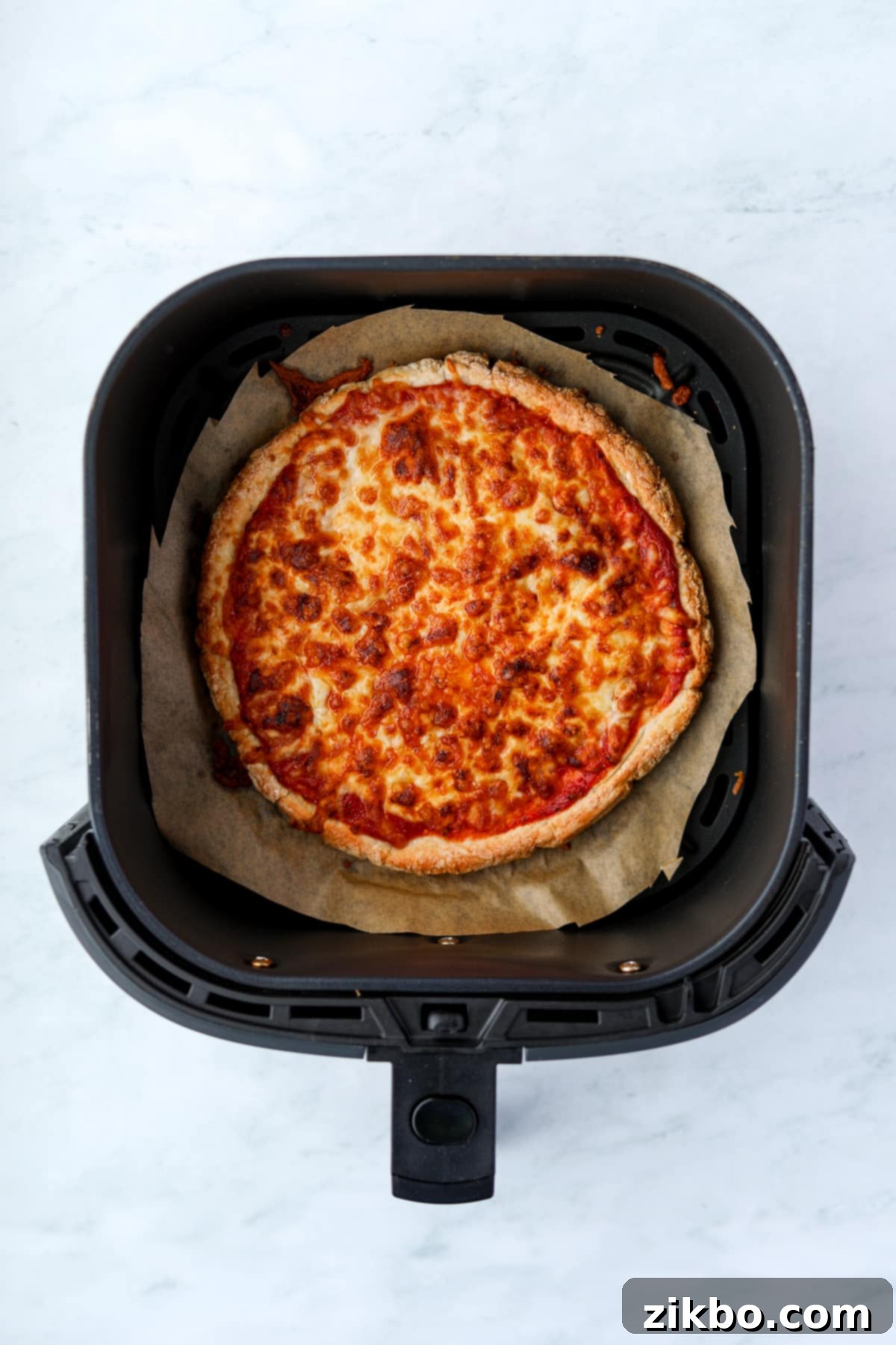 An air fryer with a cooked cheese pizza inside.
