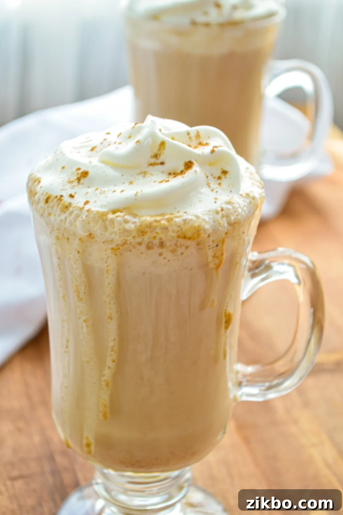 Two beautifully presented glasses of Instant Pot Pumpkin Spice Lattes, generously topped with fluffy whipped cream and a sprinkle of spices, perfectly capturing the cozy essence of fall.