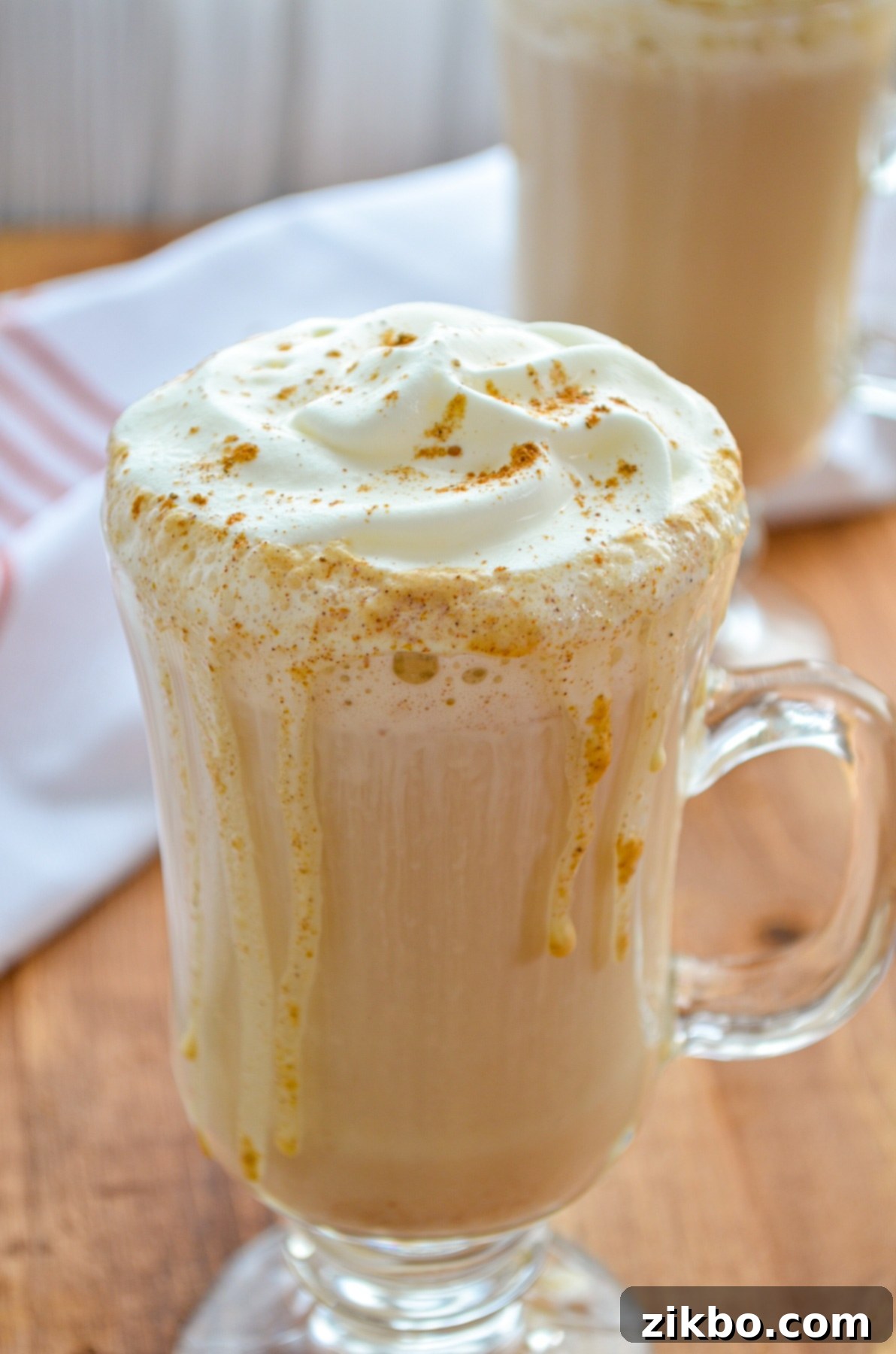 Two cozy glass mugs filled with steaming pumpkin spice lattes, elegantly topped with whipped cream, perfect for a fall morning or an evening treat.