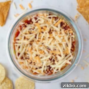 A bowl of dip with salsa, Greek yogurt, and topped with shredded cheese.