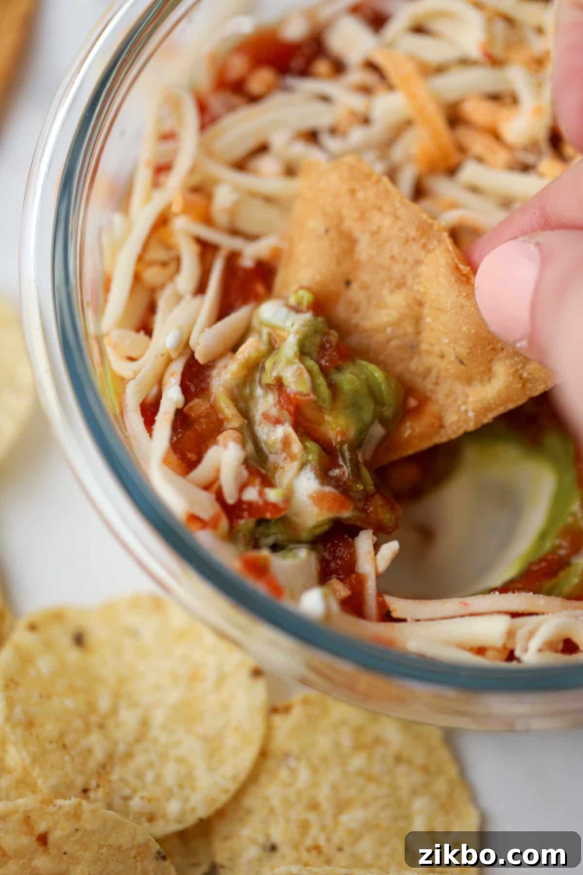 A tortilla chip being dipped into a small bowl of layered dip.