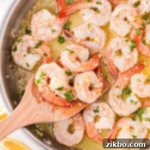 A wooden spatula scooping perfectly cooked shrimp from a skillet, rich with lemon garlic butter sauce.