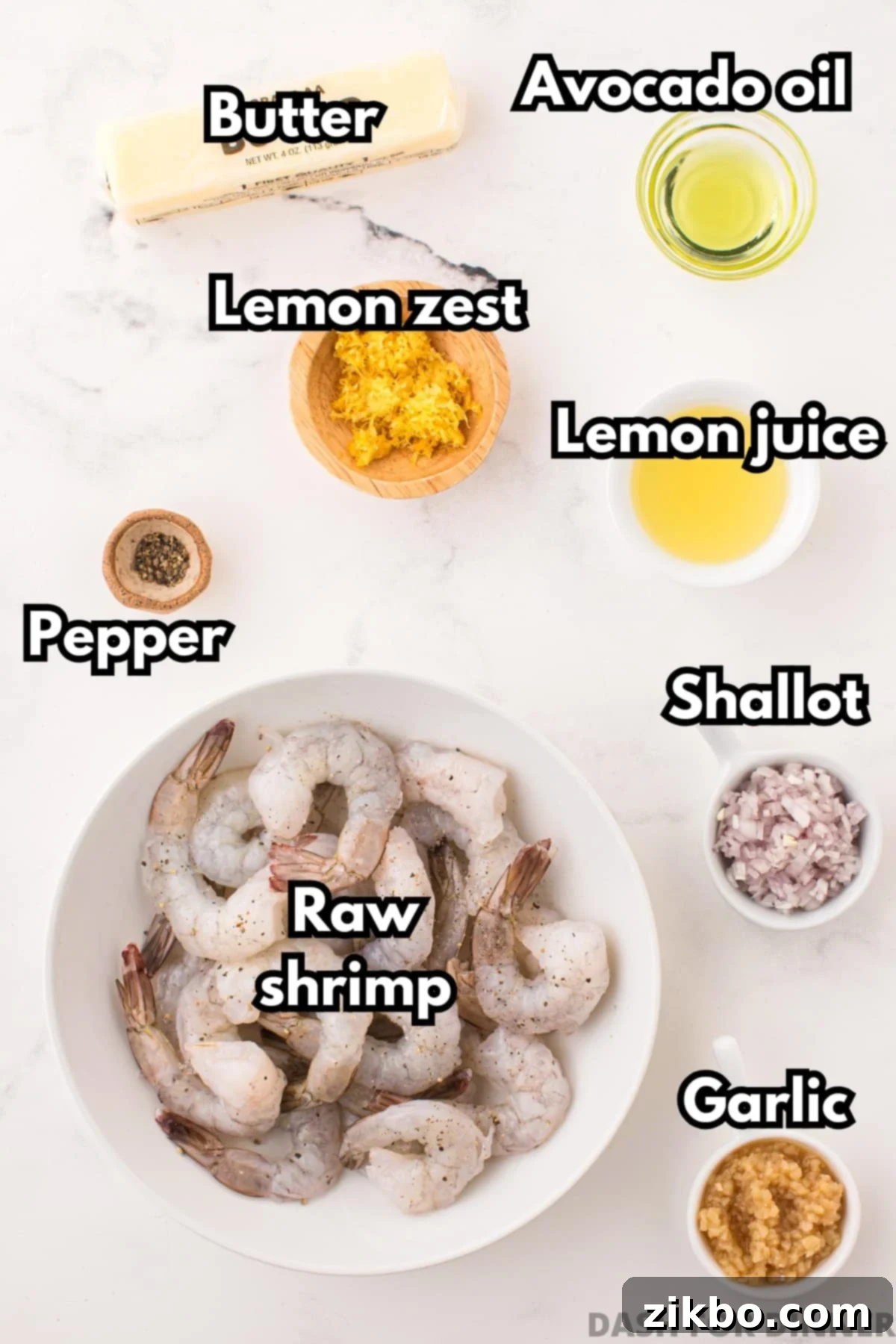 A bowl of fresh raw shrimp surrounded by minced garlic, lemon zest, butter, and other fresh ingredients.