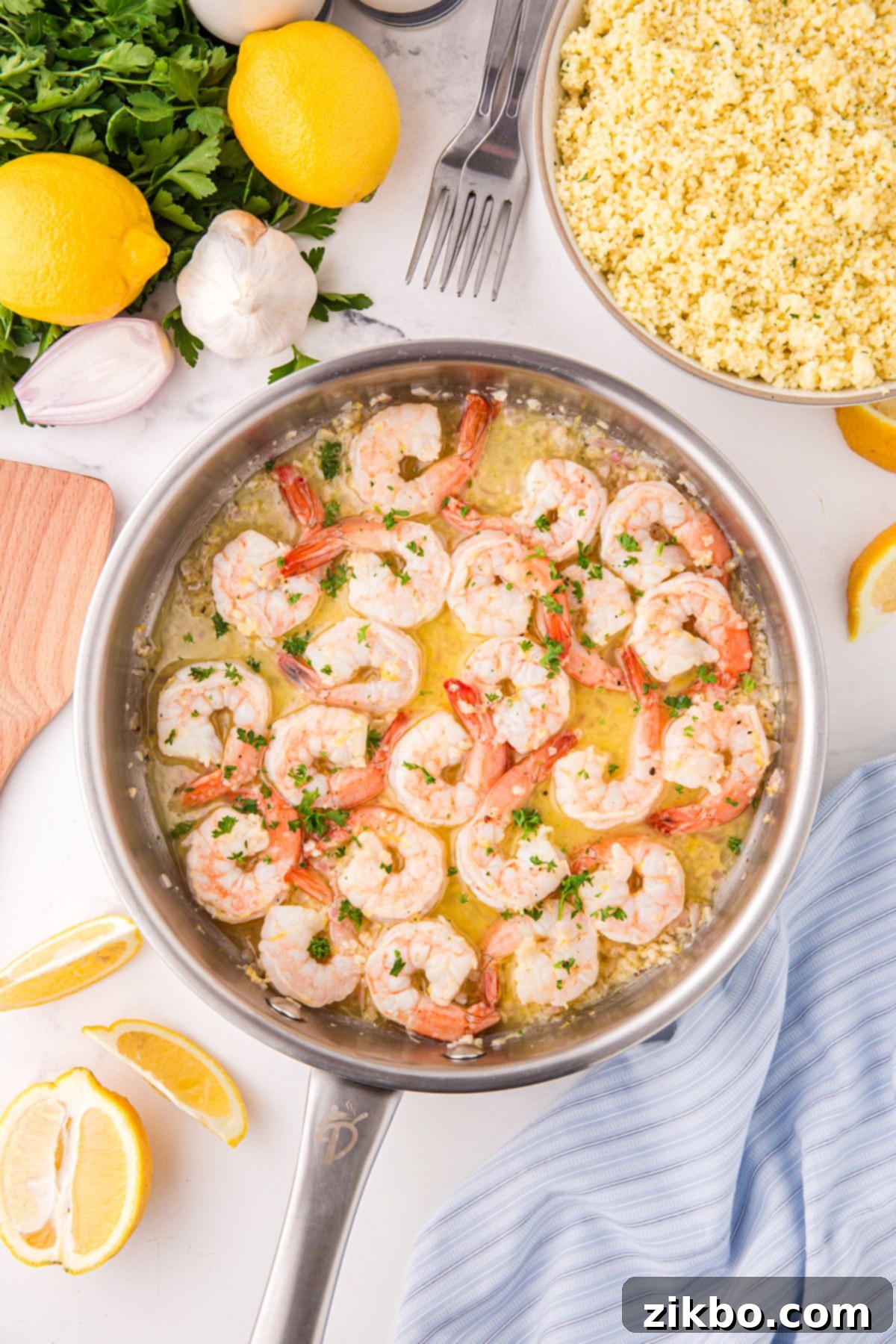 A shiny stainless steel skillet brimming with perfectly cooked lemon garlic butter shrimp, with fresh parsley and lemon wedges artfully arranged around the frame.