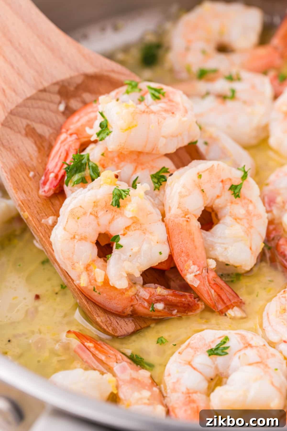 A wooden spatula gently scooping a generous portion of cooked shrimp from a sizzling skillet, showcasing the golden garlic butter sauce.