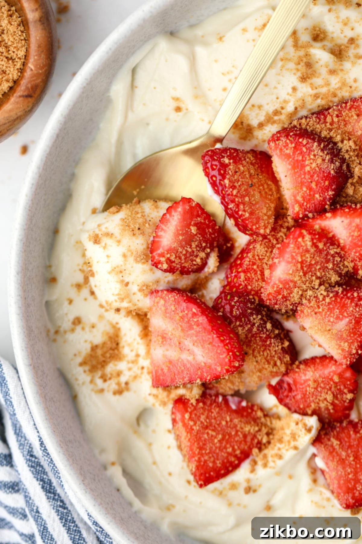 A spoon taking a portion of yogurt from a bowl topped with strawberries.