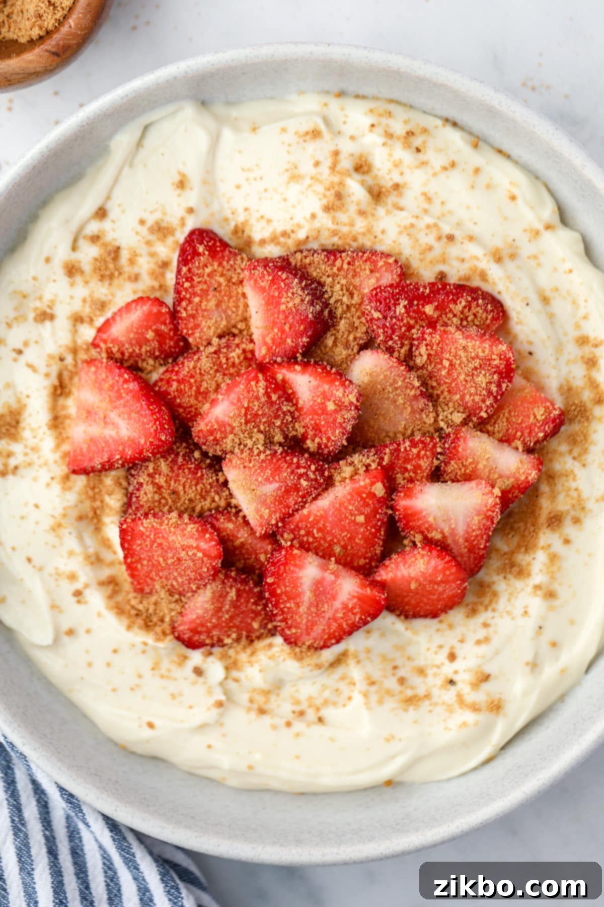 A bowl filled with yogurt, fresh strawberries, and graham cracker crumbs.
