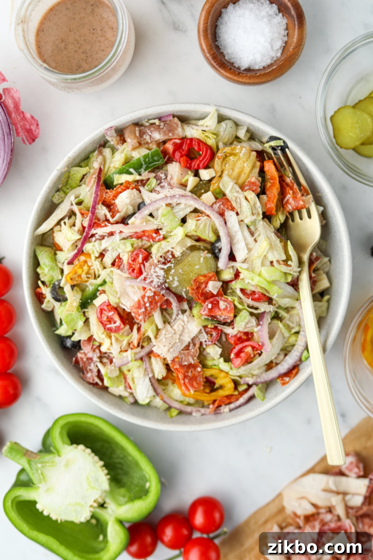 A vibrant bowl of Italian Sub Salad, showcasing crisp lettuce, colorful deli meats, cheeses, and various toppings like pickles, red onion, and a sprinkle of Parmesan cheese.