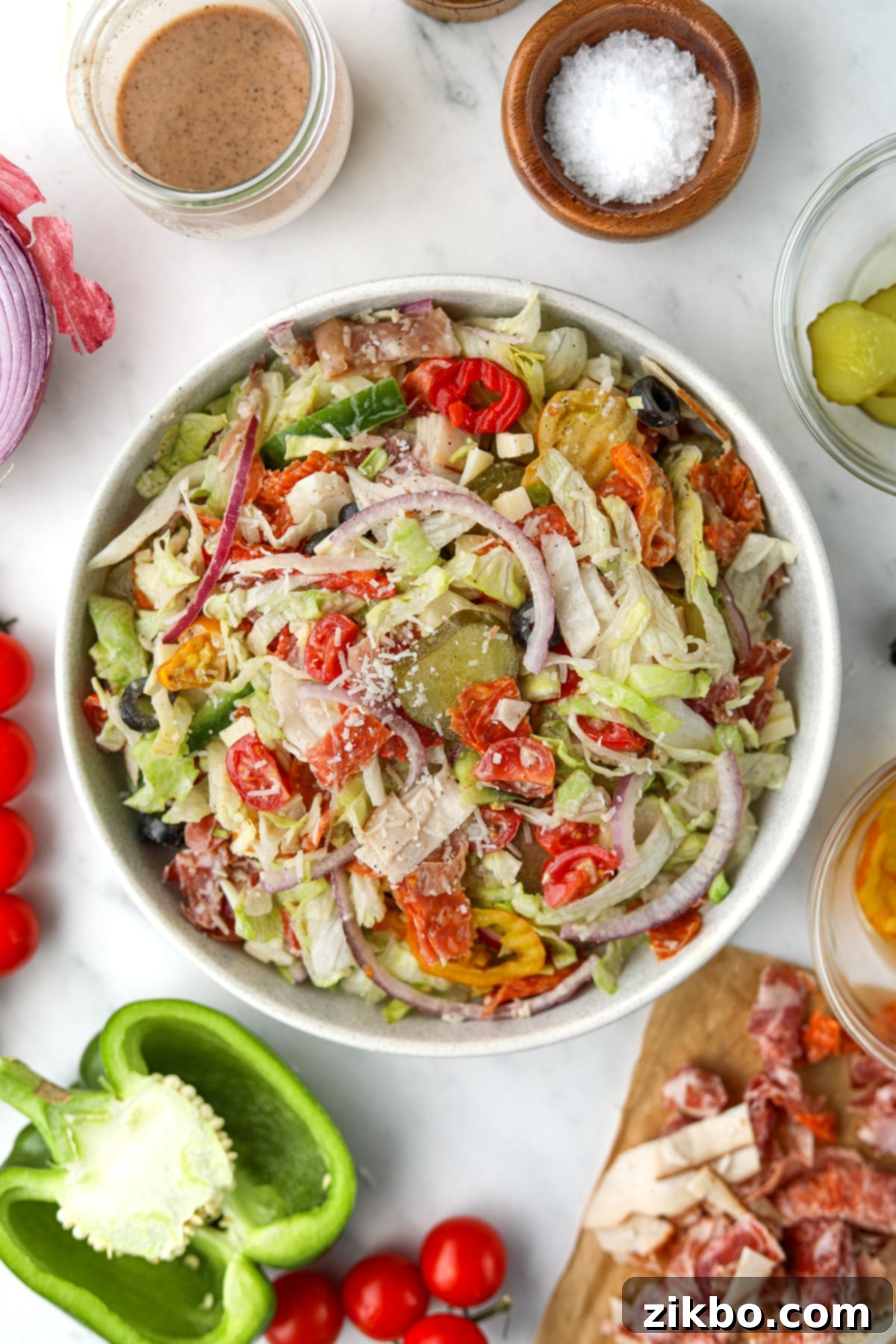 An overhead image of a large, freshly prepared Italian Sub Salad in a bowl, surrounded by various fresh vegetables and deli meat, highlighting the colorful array of ingredients.