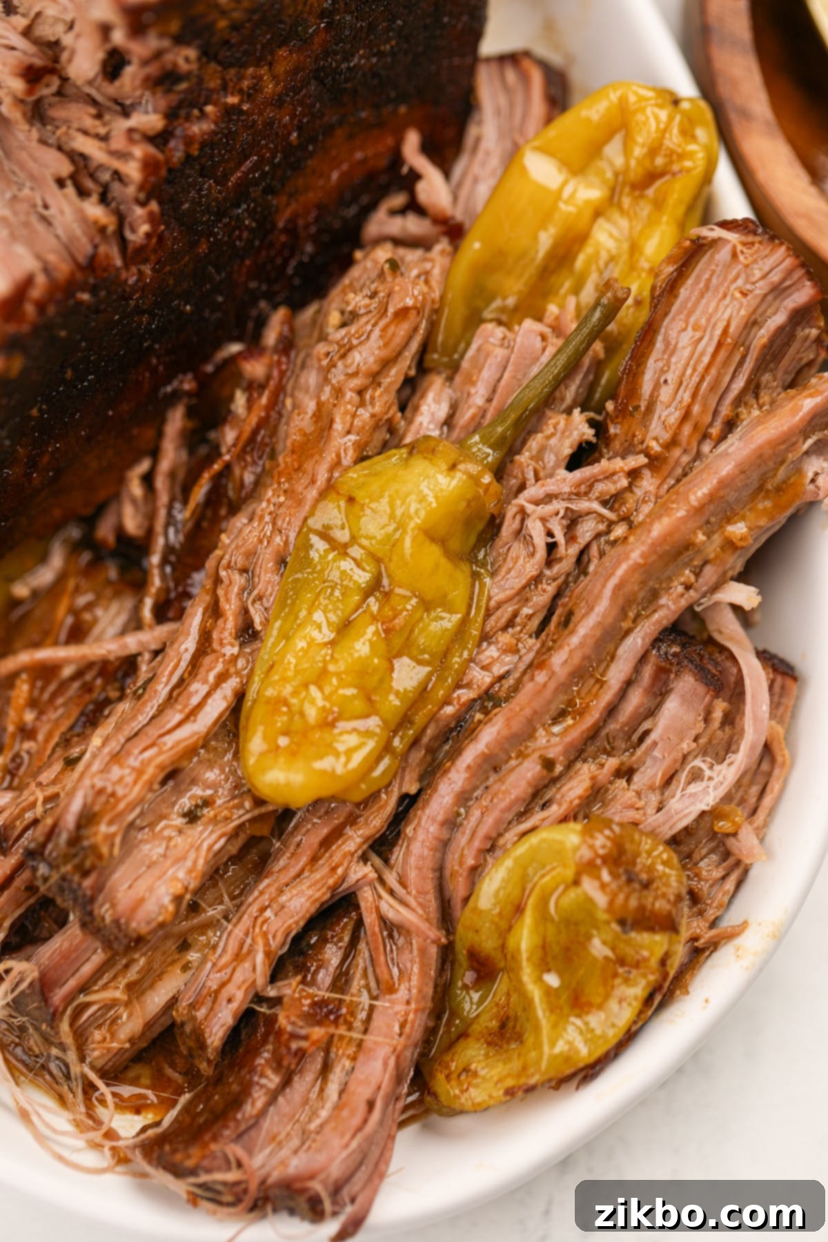 Shredded pot roast with cooked pepperoncini peppers alongside it.