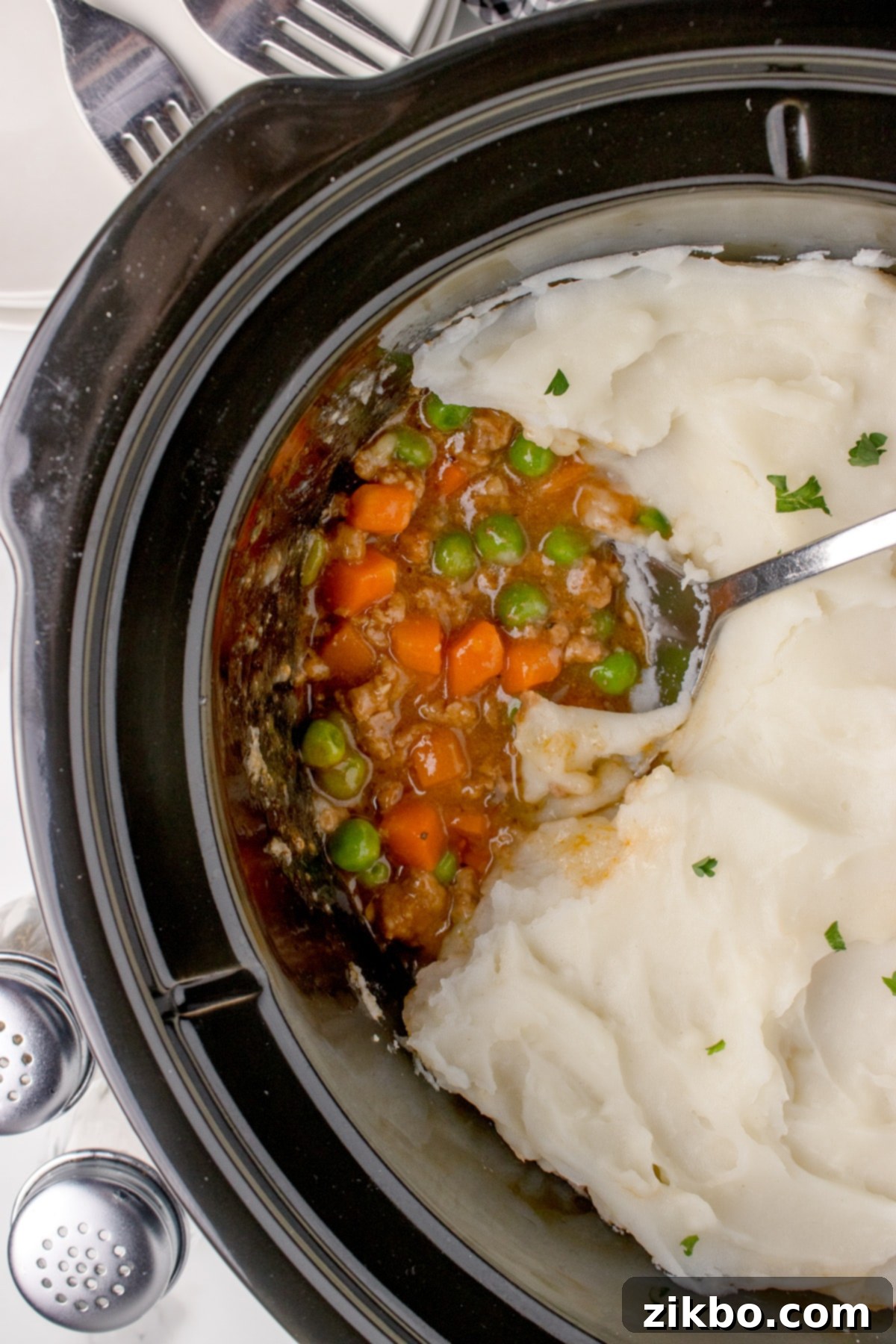 A slow cooker filled with hearty cottage pie, elegantly topped with creamy mashed potatoes and ready to serve.