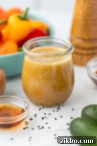 A charming small glass jar, tightly sealed with a lid, containing the freshly prepared ginger sesame dressing, ready for refrigeration.