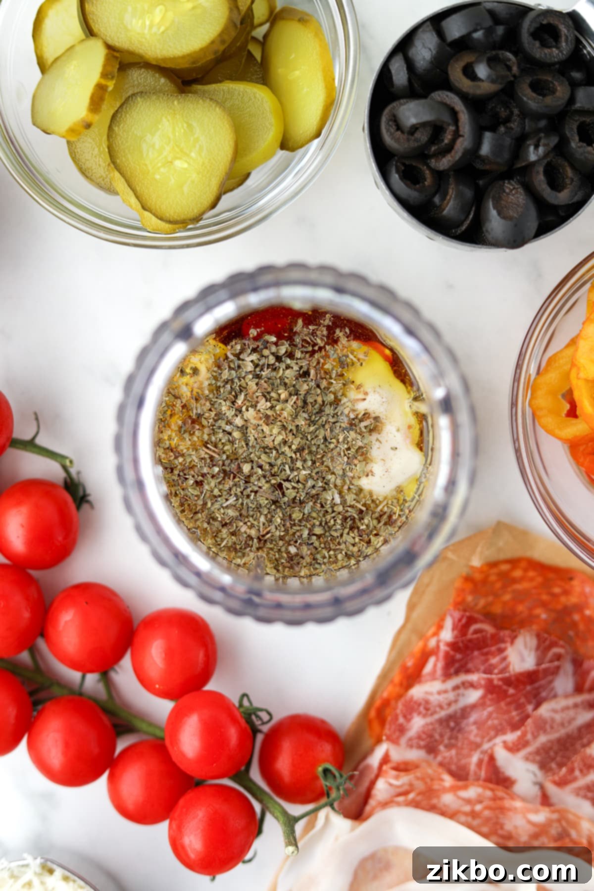 A clear glass jar blender filled with olive oil, dried oregano, red wine vinegar, and other vibrant dressing ingredients before they are combined.