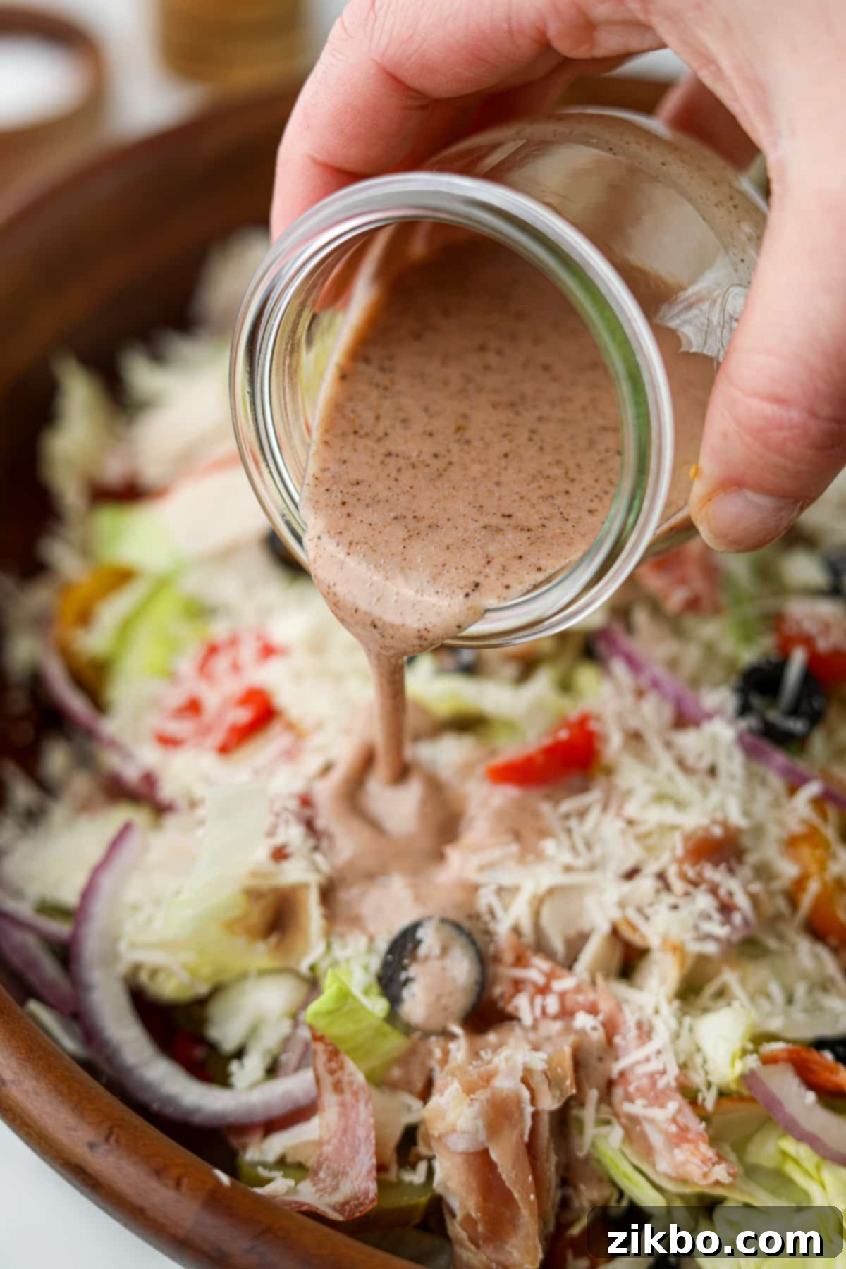 A luscious stream of homemade sub sauce drizzling gracefully over a vibrant chopped salad, replete with crisp red onion, ripe tomato slices, and fresh green lettuce, highlighting its perfect texture and visual appeal.