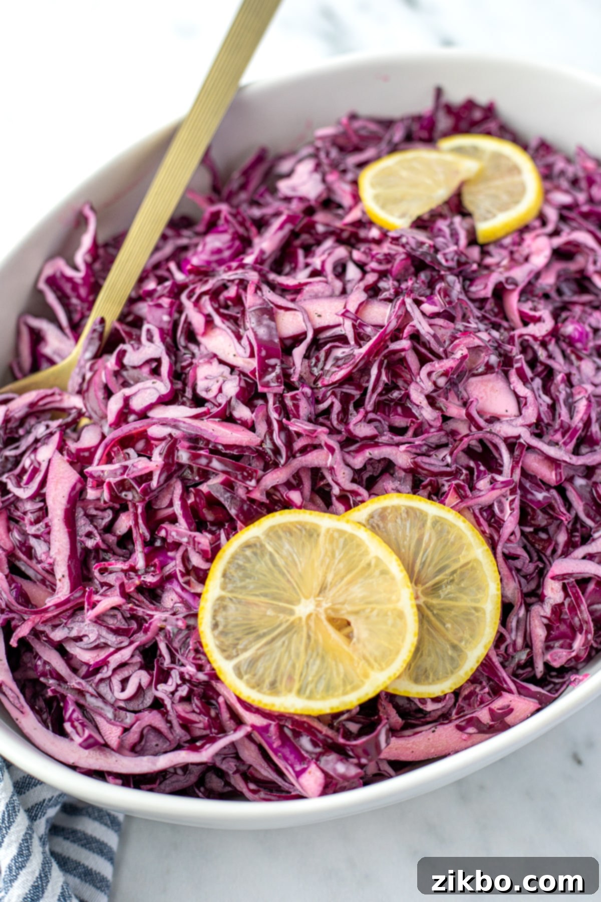 Zesty Israeli Cabbage Slaw 11 A spoon resting along the side of an oval bowl filled with vibrant red cabbage salad, showcasing its appealing texture and color.