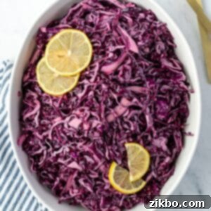 Zesty Israeli Cabbage Slaw 12 An oval bowl filled with vibrant red cabbage salad and garnished with fresh lemon slices, ready for serving.