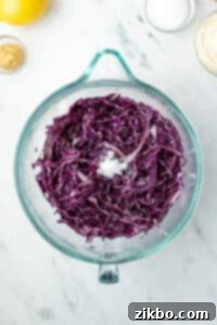 A large glass bowl filled with shredded red cabbage, seasoned and resting, ready for the next step.