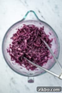 Creamy dressing being drizzled over shredded red cabbage in a bowl, ready for tossing.