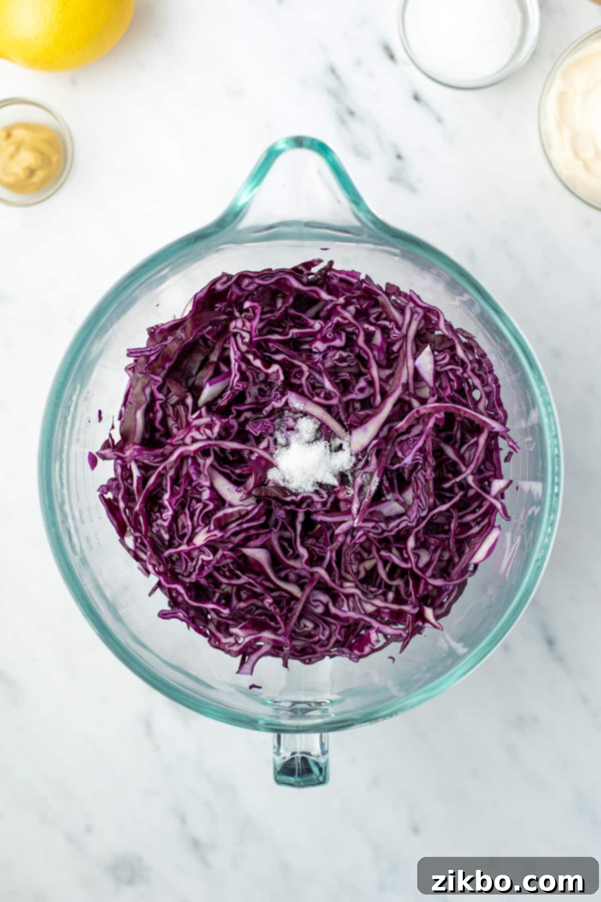 Zesty Israeli Cabbage Slaw 5 A large glass bowl filled with finely shredded red cabbage, seasoned and resting.