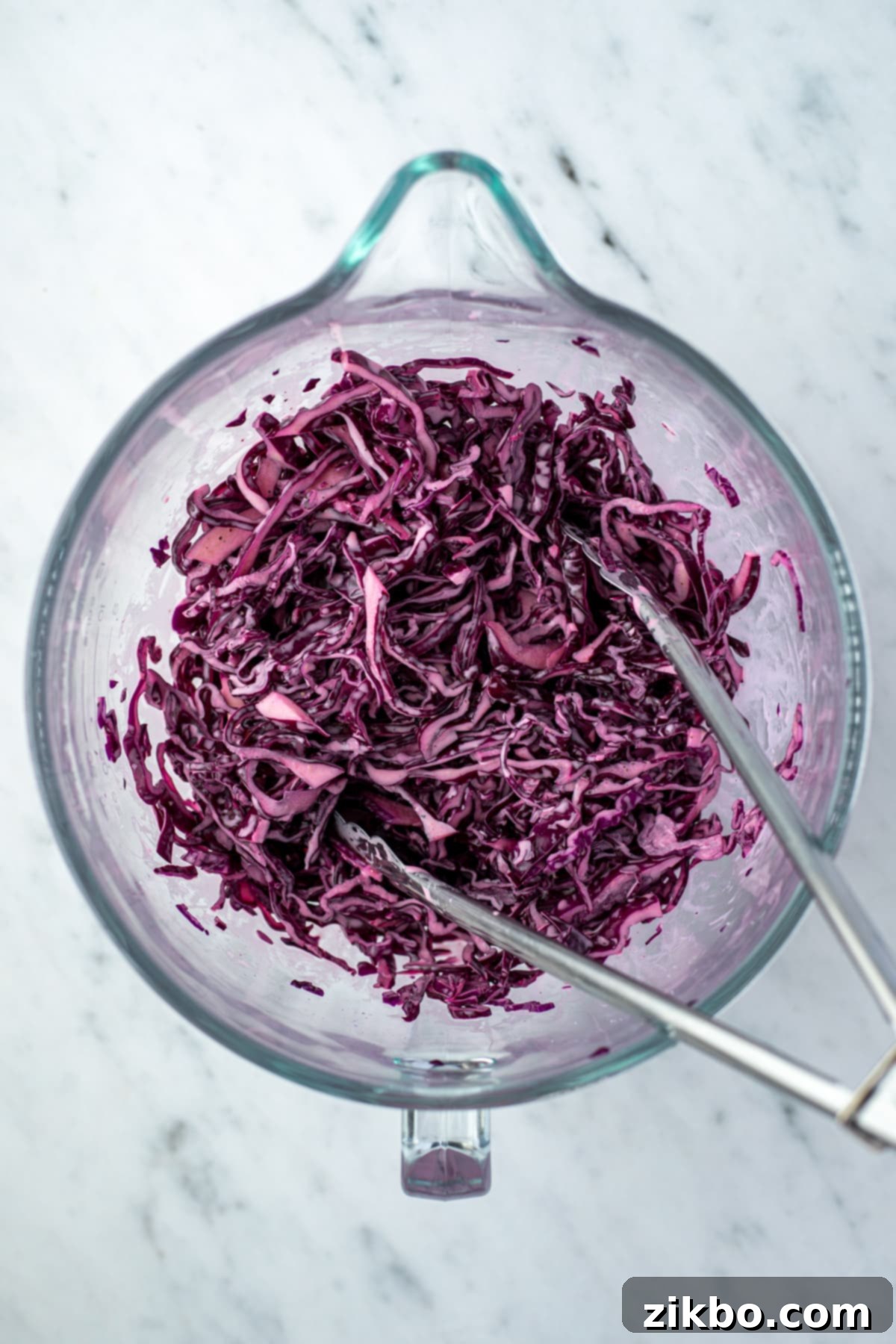 Zesty Israeli Cabbage Slaw 8 Creamy dressing being drizzled over a large bowl of shredded red cabbage, ready to be tossed.